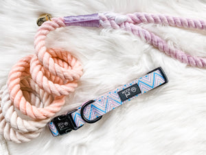 Showcasing flat lay image of Pink, Blue and Gold Chevron pattern Dog Collar with metal D ring in black colour from Woof First. The Collar sitting on the tri-colour rope leash in colour pink, purple and grey.