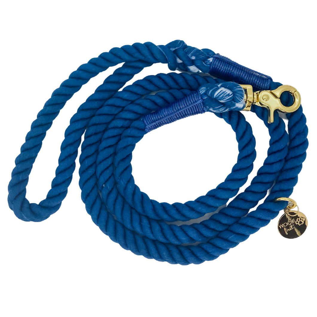 The image shown is of the Dogs Rope Leash in Dark Blue colour. The rope leash has gold metal hardware finishes and has Woof First imprinted on a round charm.